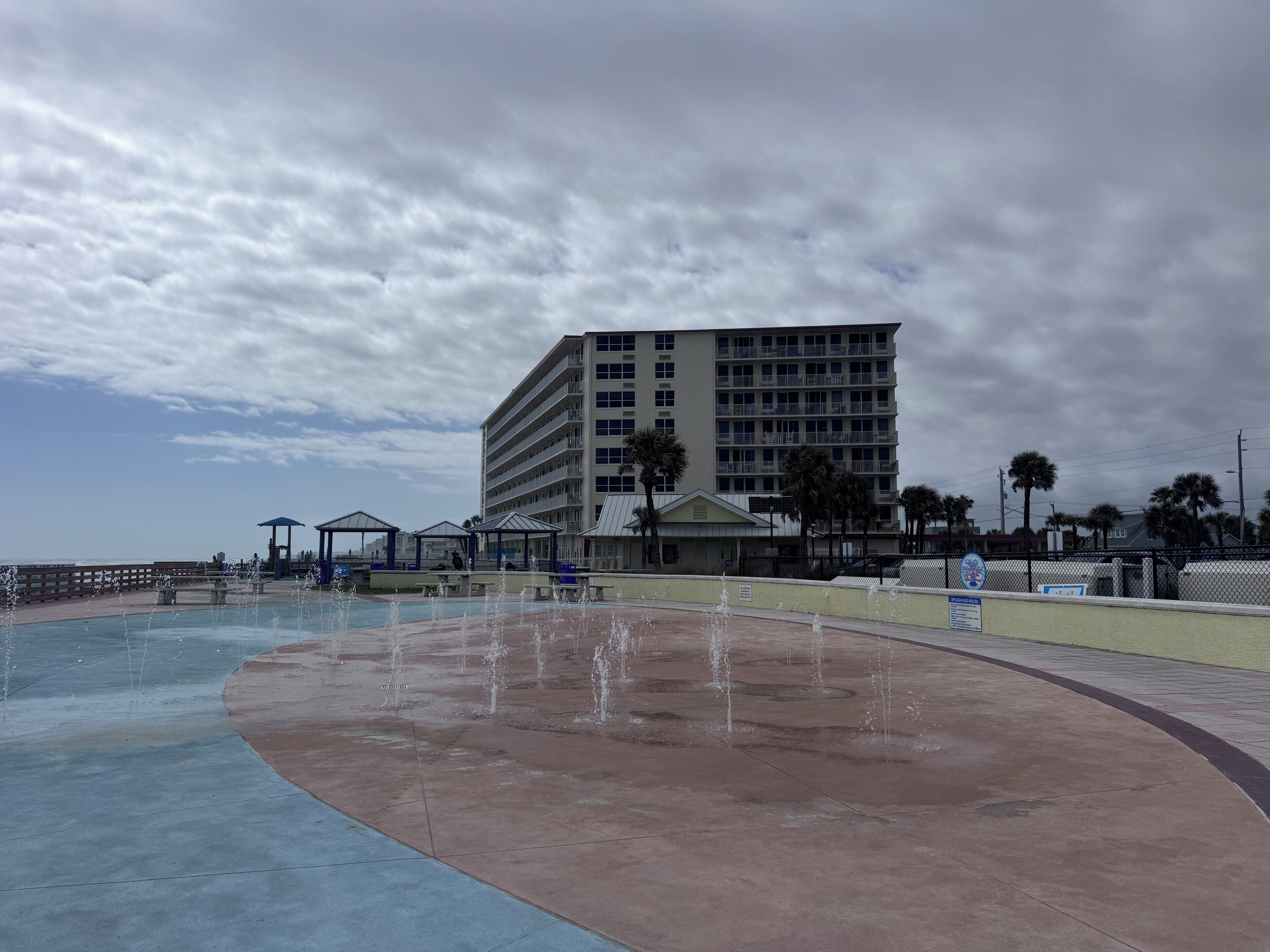 Una piscina con fuentes, una zona de playa y un gran edificio de hotel al fondo.