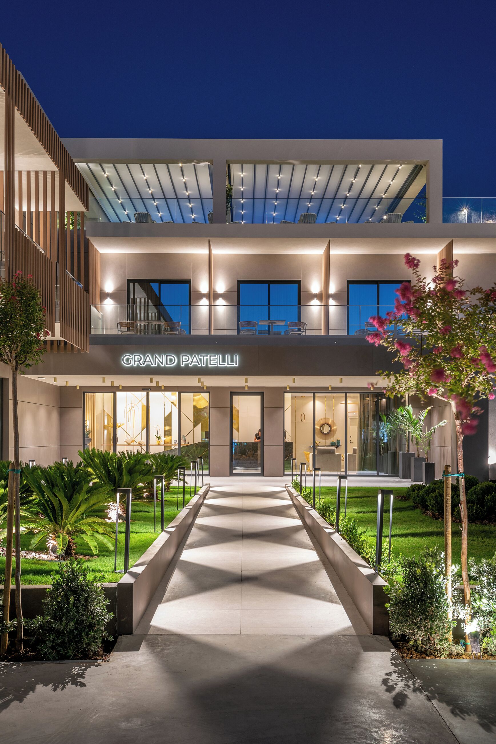 A modern hotel with a prominent entrance, a covered outdoor seating area, and a well-maintained garden.