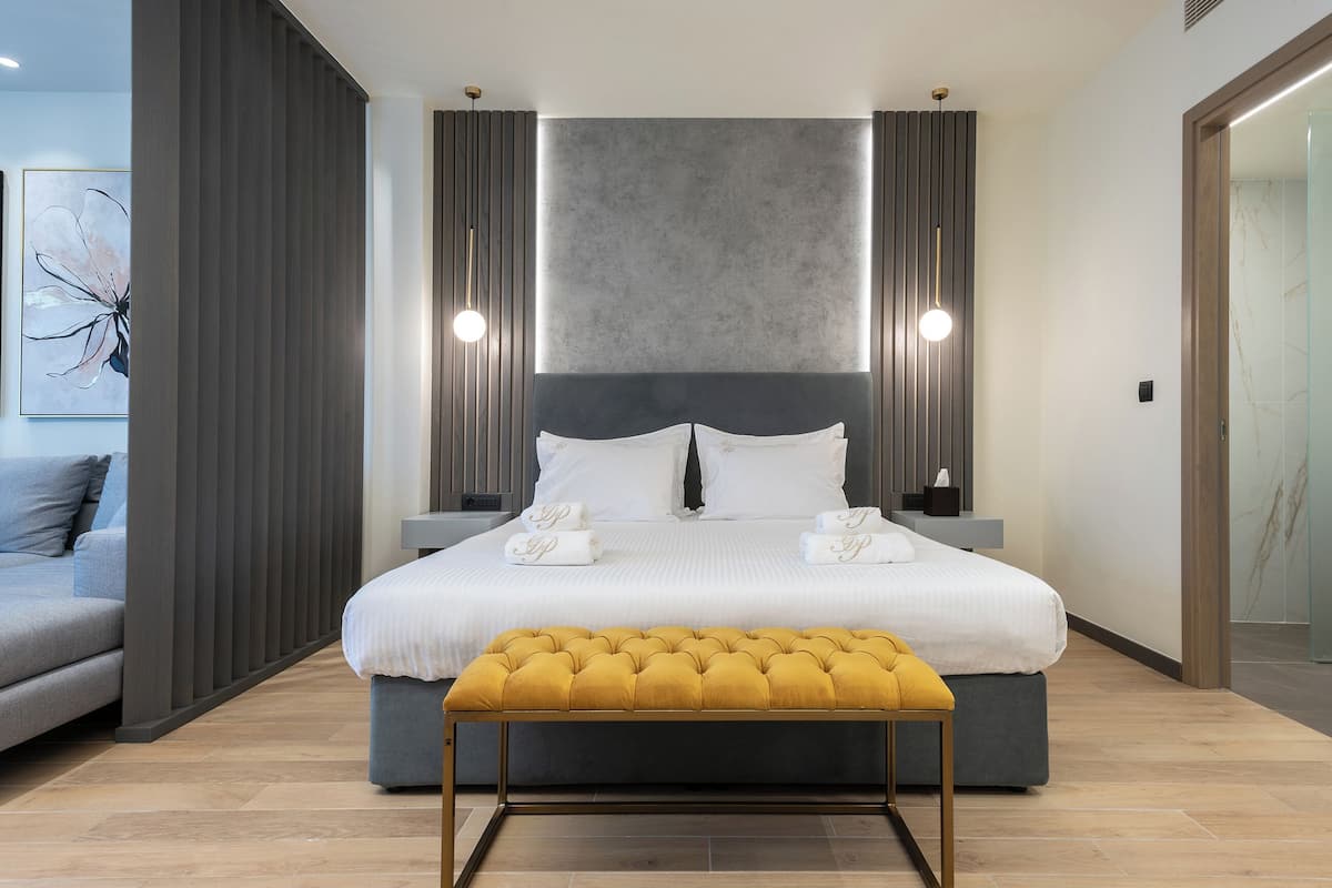 A modern bedroom with a large bed, bedside tables, a bench, and a wall-mounted light fixture.