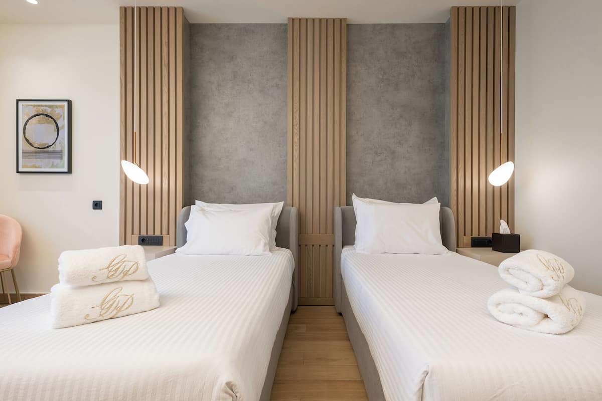 A hotel room with two beds, a wooden accent wall, a framed artwork, and a bedside table with a lamp.