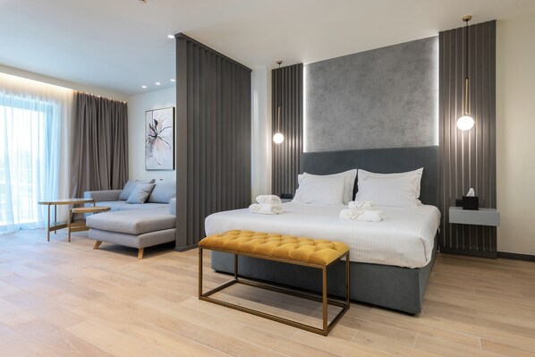 A modern hotel room with a large bed, a sofa, a small table, and a bench. - Grand Patelli (Lemnos)