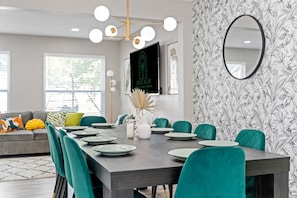 Un comedor con una mesa larga, sillas color turquesa y un candelabro moderno.