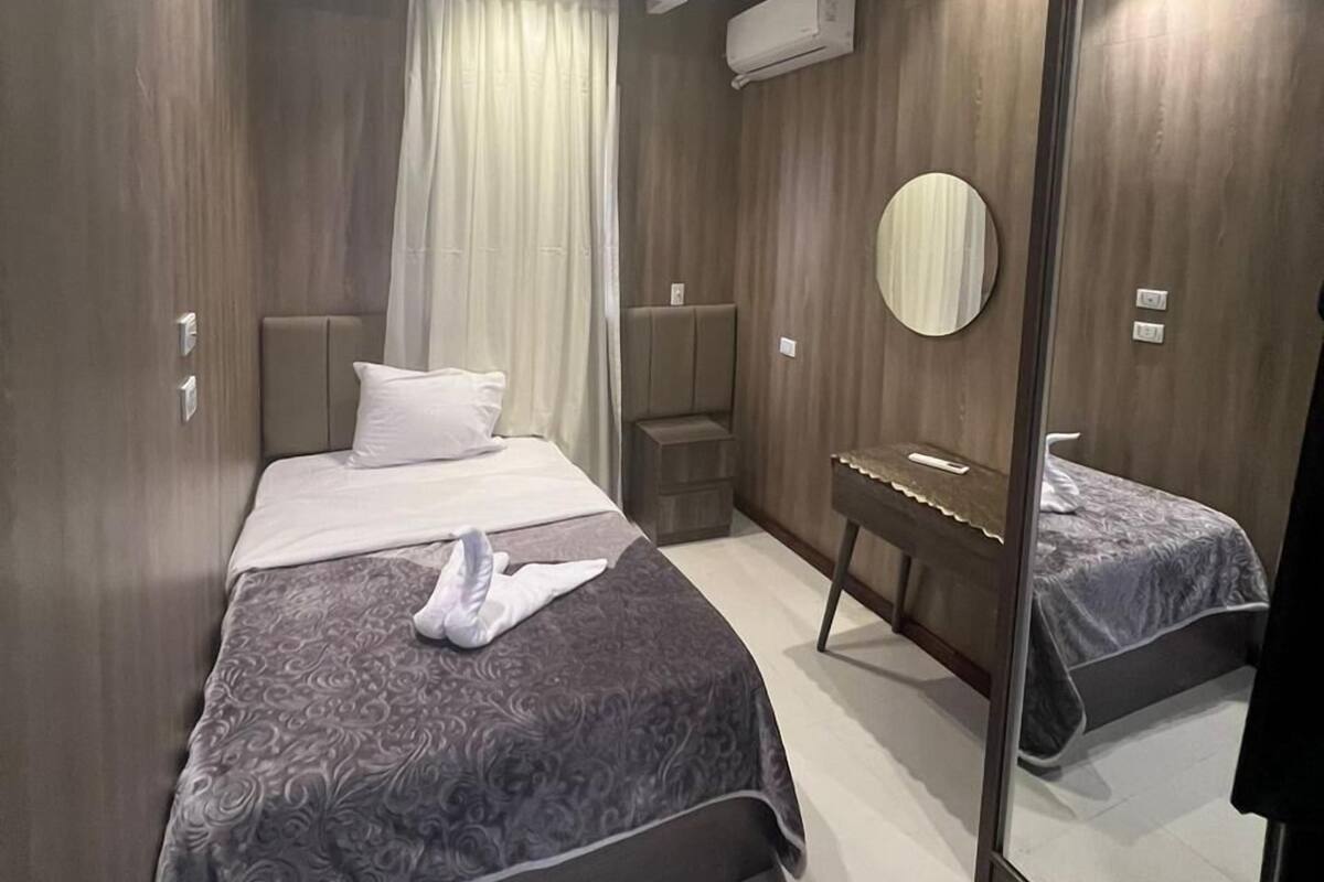 A modern bedroom with a bed, bedside tables, a mirror, and an air conditioning unit.