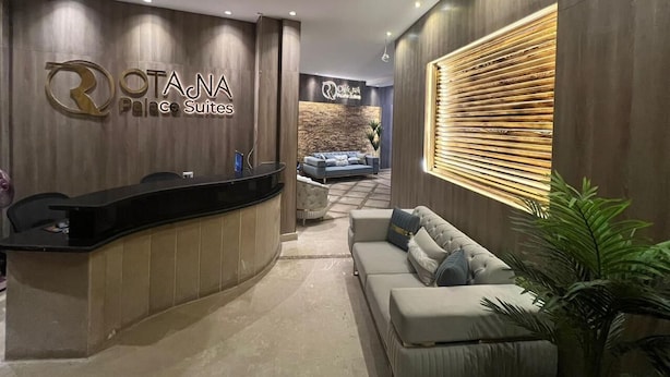 A reception area with a reception desk, a sofa, and a wall with a wooden panel design. - Rotana Palace Suites (Cairo)