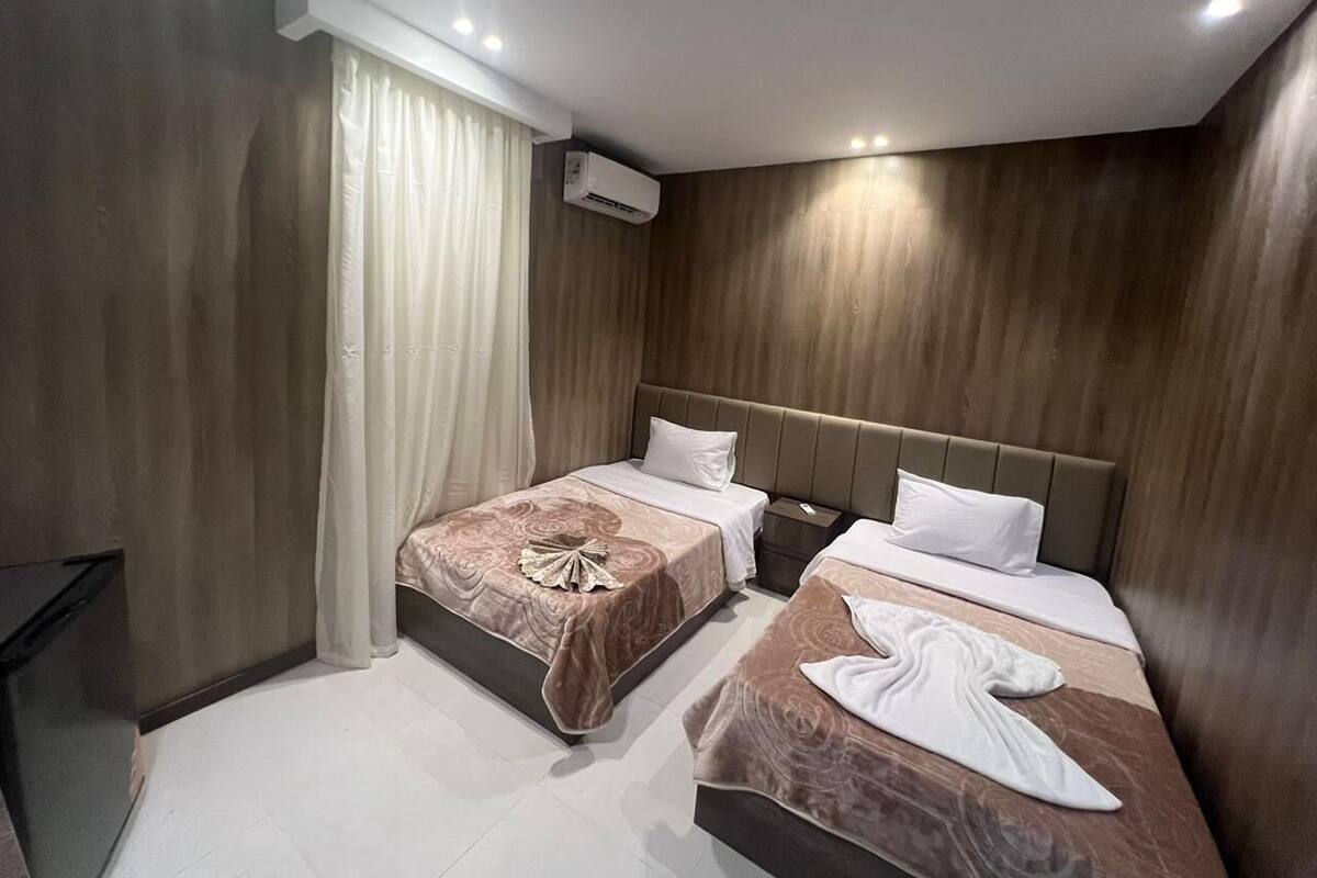 A hotel room with two beds, a flat-screen TV, and an air conditioning unit.