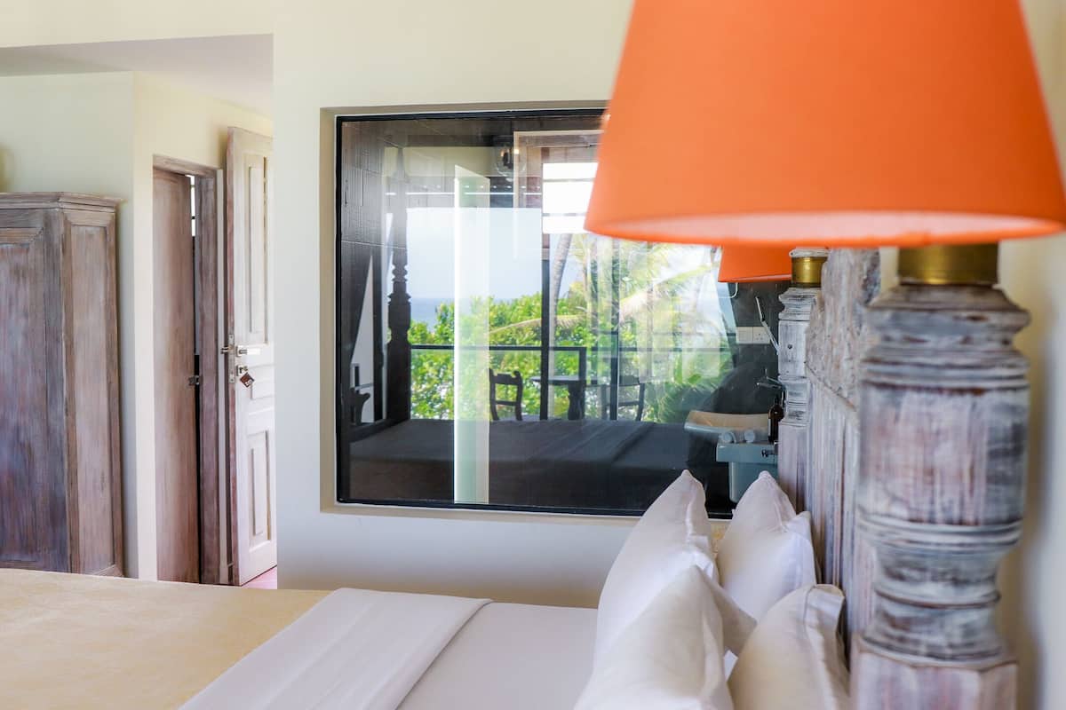 A hotel room with a bed, a window with a view of greenery, and a wooden wardrobe.