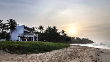 Una propiedad frente a la playa con un edificio blanco, palmeras y una playa de arena.