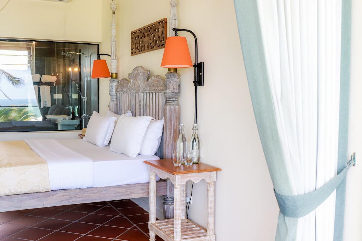 A hotel room with a bed, a nightstand, a wall-mounted lamp, and a window with curtains.