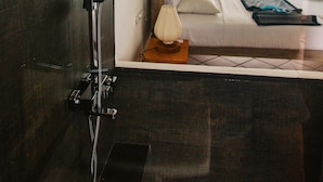 A modern bathroom with a shower, a visible bed with a view of palm trees, and a mounted camera on the wall. - Naomi Beach Resort (Weligama)