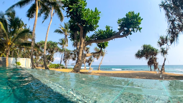 A clear pool with a view of a beach and palm trees. - Naomi Beach Resort (Weligama)