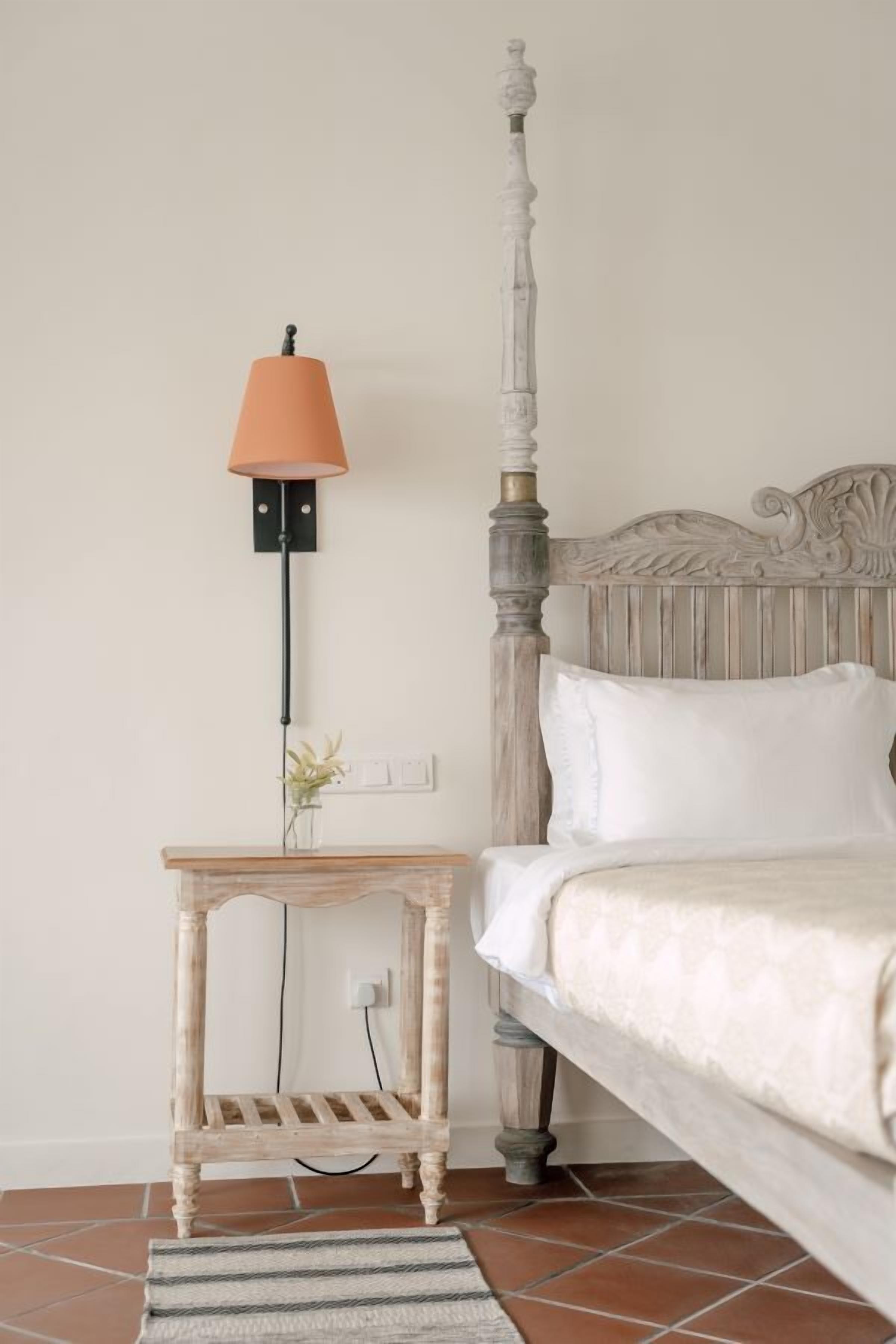 A bedroom with a four-poster bed, a bedside table with a lamp, and a small plant.