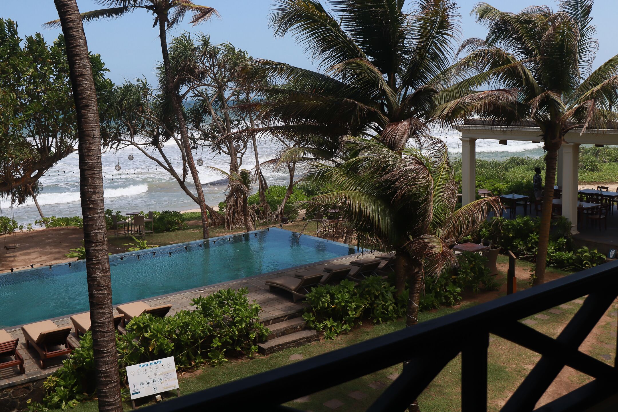 A pool with lounge chairs, palm trees, and a view of the ocean.