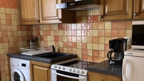 Une cuisine compacte équipée d’un lave-linge, d’une cuisinière, d’un four à micro-ondes et d’une machine à café.