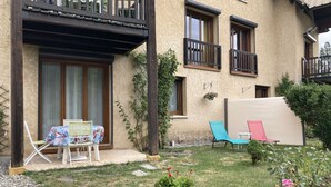 Un immeuble résidentiel doté d’un balcon, d’un petit jardin avec des chaises et des plantes en pot, et offrant une vue dégagée sur les environs.