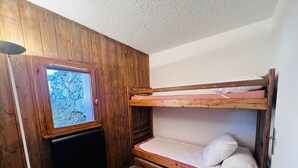 Una habitación pequeña con paredes de madera, una cama litera, un televisor y una ventana con vistas a árboles.
