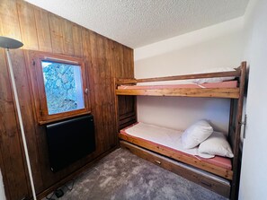 Piccola stanza con pareti in legno, un letto a castello, una televisione e una finestra vista alberi.
