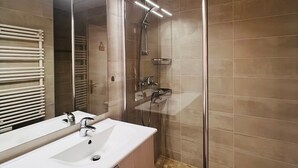 Un baño moderno con cabina de ducha de vidrio, un espejo grande y un lavamanos blanco.