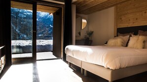 Ein Schlafzimmer mit einem großen Bett, Holzboden und Blick auf eine verschneite Landschaft durch eine Glastür.