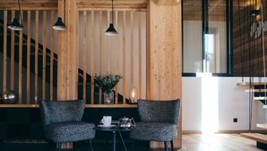 Ein modernes Interieur mit Holzvertäfelung, zwei Polsterstühlen, einem kleinen Tisch mit Teekanne und Tasse, einem weißen Fellteppich und Pendelleuchten.