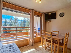 A room with a bed, a dining table with chairs, a TV mounted on the wall, and a large window with curtains. - Comfortable Studio · 4 people · Flaine Center · Terrace (Flaine)