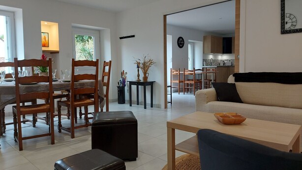 Un grand espace de vie comprenant une table à manger, des chaises, un canapé et, au fond, une cuisine.