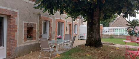 A brick building with a glass table and chairs, a tree, and a small garden area.