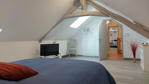Une chambre avec un plafond en pente, un lit, une télévision, un bureau et une armoire.