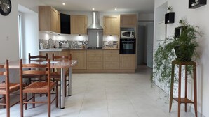 Une cuisine moderne avec des meubles en bois, une hotte en acier inoxydable, un four à micro-ondes et un four traditionnel. On y trouve une table à manger avec des chaises et une plante en pot, placée sur un support.