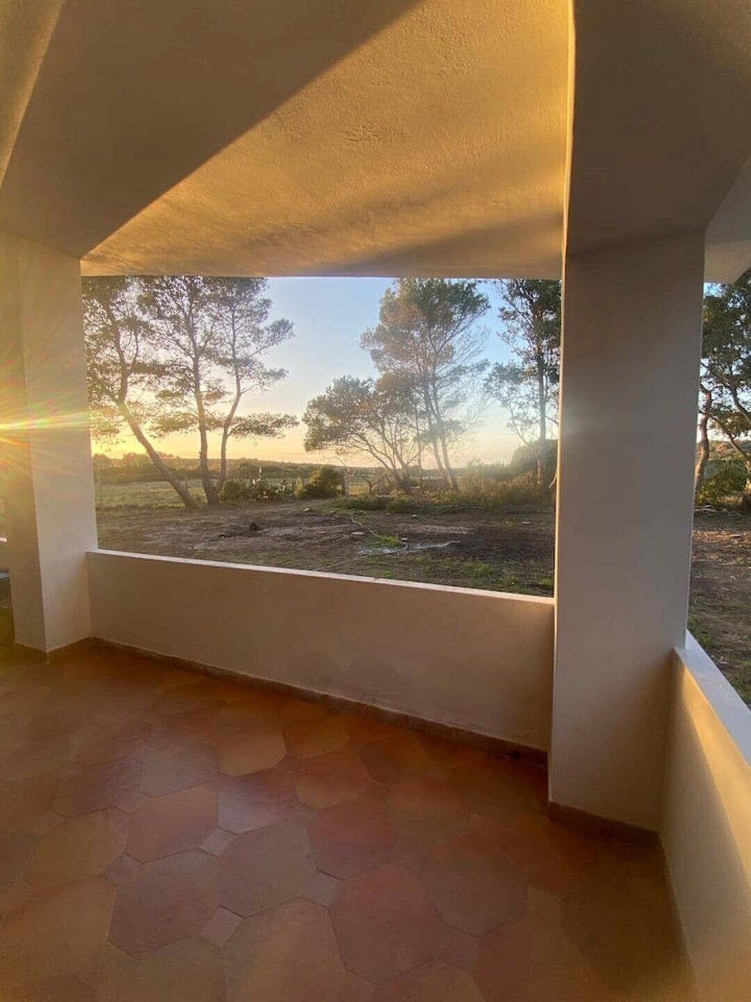 A room with a large window overlooking a natural landscape with trees and a clear sky.