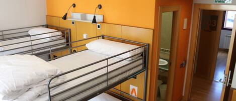 A dormitory room with bunk beds, a small shelf with a lamp, and a door leading to a bathroom.