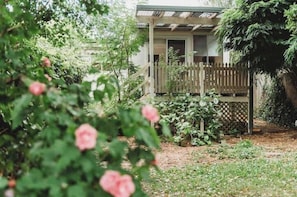 Une maison avec une terrasse en bois, une cour clôturée et un jardin agrémenté de fleurs roses.