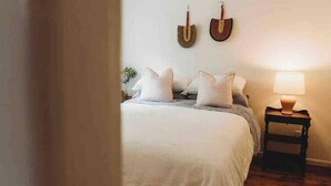 Un dormitorio con cama, almohadas, una mesita de noche y decoración en la pared.