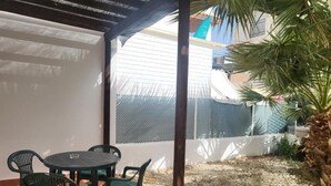 Pihalla on pyöreä pöytä ja tuolit, pergola sekä aidattu alue, jossa kasvaa palmu.