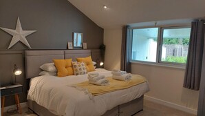 A bedroom with a large bed, a star decoration on the wall, a bedside table with a lamp, and a window with curtains. - Hazel (Newton Abbot)