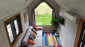 A cozy room with a sofa, a chair, a colorful striped rug, a potted plant, and a TV mounted on the wall. - The Tiny House (Newton Abbot)