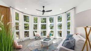 A modern living room with a curved ceiling, large windows, a ceiling fan, a white sofa, a coffee table, and a round rug.