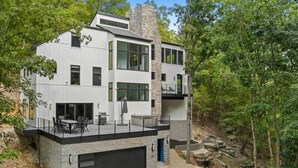 A modern two-story house with a stone facade, large windows, and a balcony with outdoor furniture.