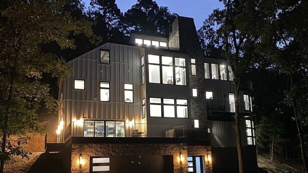 A modern two-story house with a stone facade, large windows, and a well-lit entrance.