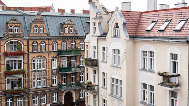 A row of multi-story buildings with ornate facades, large windows, and balconies with flower boxes.