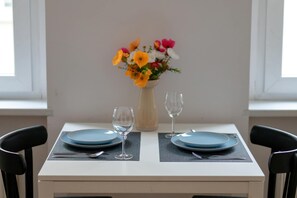 A dining table with two blue plates, two wine glasses, and a vase of flowers. - Cozy Apartment in the City Center | Near the Old Market Square (Poznań)