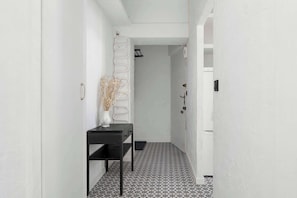 Un couloir avec un sol à carreaux noirs et blancs, un mur blanc et une console noire sur laquelle est posé un vase contenant des plantes séchées.