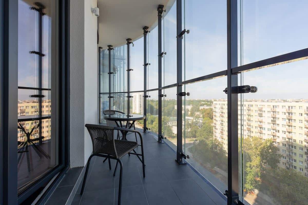 Ein Balkon mit Tisch und Stühlen, große Fenster und Blick auf Gebäude und Bäume.