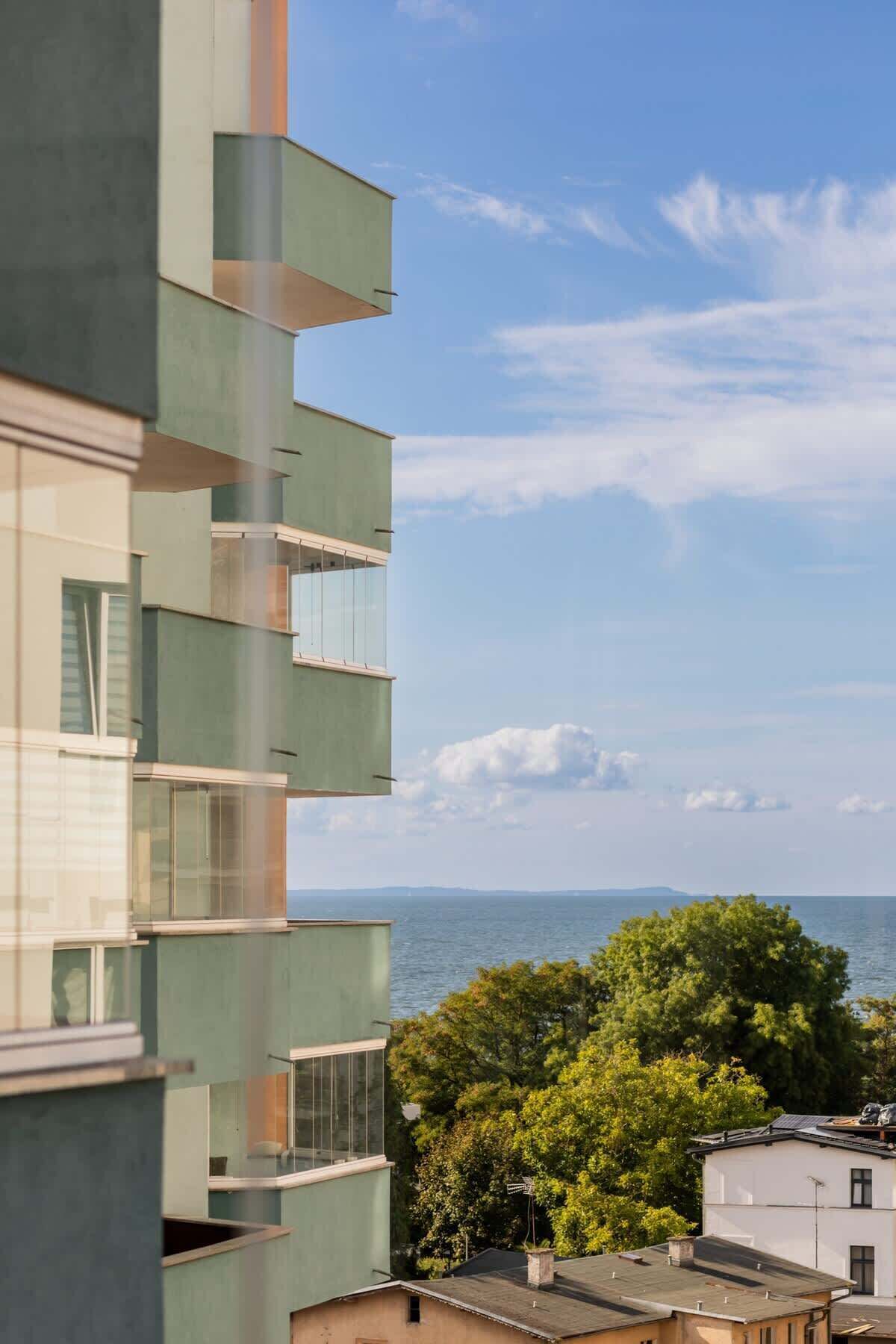 Ein modernes Gebäude mit mehreren Balkonen und Blick auf Wasser und Grünflächen.