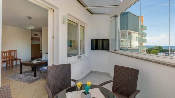 Un balcon avec des fauteuils en osier, une petite table et un téléviseur fixé au mur.