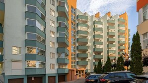 Un immeuble résidentiel à plusieurs étages, doté de balcons, d’un espace de stationnement et offrant une vue sur un ciel dégagé.