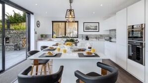 Una cocina moderna con una isla central, taburetes de bar y una mesa de comedor preparada para el desayuno.