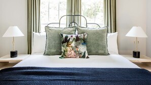 A neatly made bed with a floral pillow, two bedside lamps, and a view of greenery through the window. - Aquarius Rising (Atlanta)