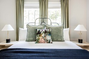A neatly made bed with a floral pillow, two bedside lamps, and a view of greenery through the window. - Aquarius Rising (Atlanta)
