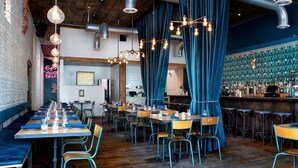 A restaurant with long communal tables, blue curtains, and a bar area with stools. - Aquarius Rising (Atlanta)