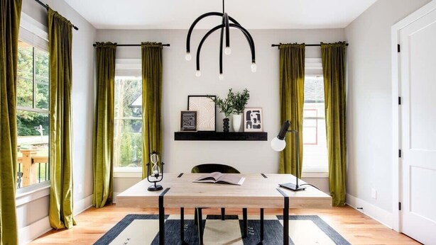 A dining area with a wooden table, black metal legs, a black and white striped rug, green curtains, and a pendant light with bulbs. - Aquarius Rising (Atlanta)